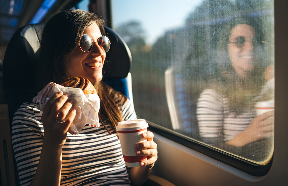 Lachende junge Frau mit Kaffee to go und Nussschnecke im Zug